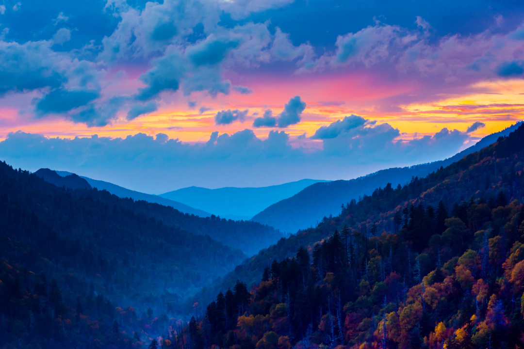 A beautiful sunset with blue fluffy clouds and a pink and gold sky. In the foreground many large hills that become less defined as they stretch out to the horizon.