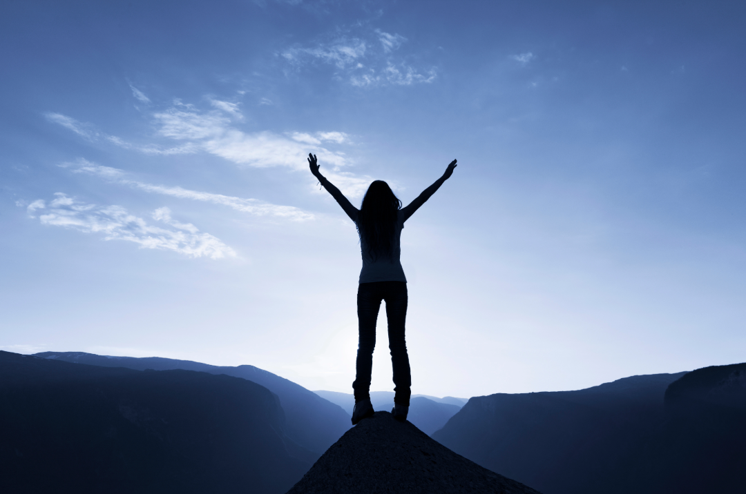 Silhouette of a woman standing victorious on the summit of a mountain.