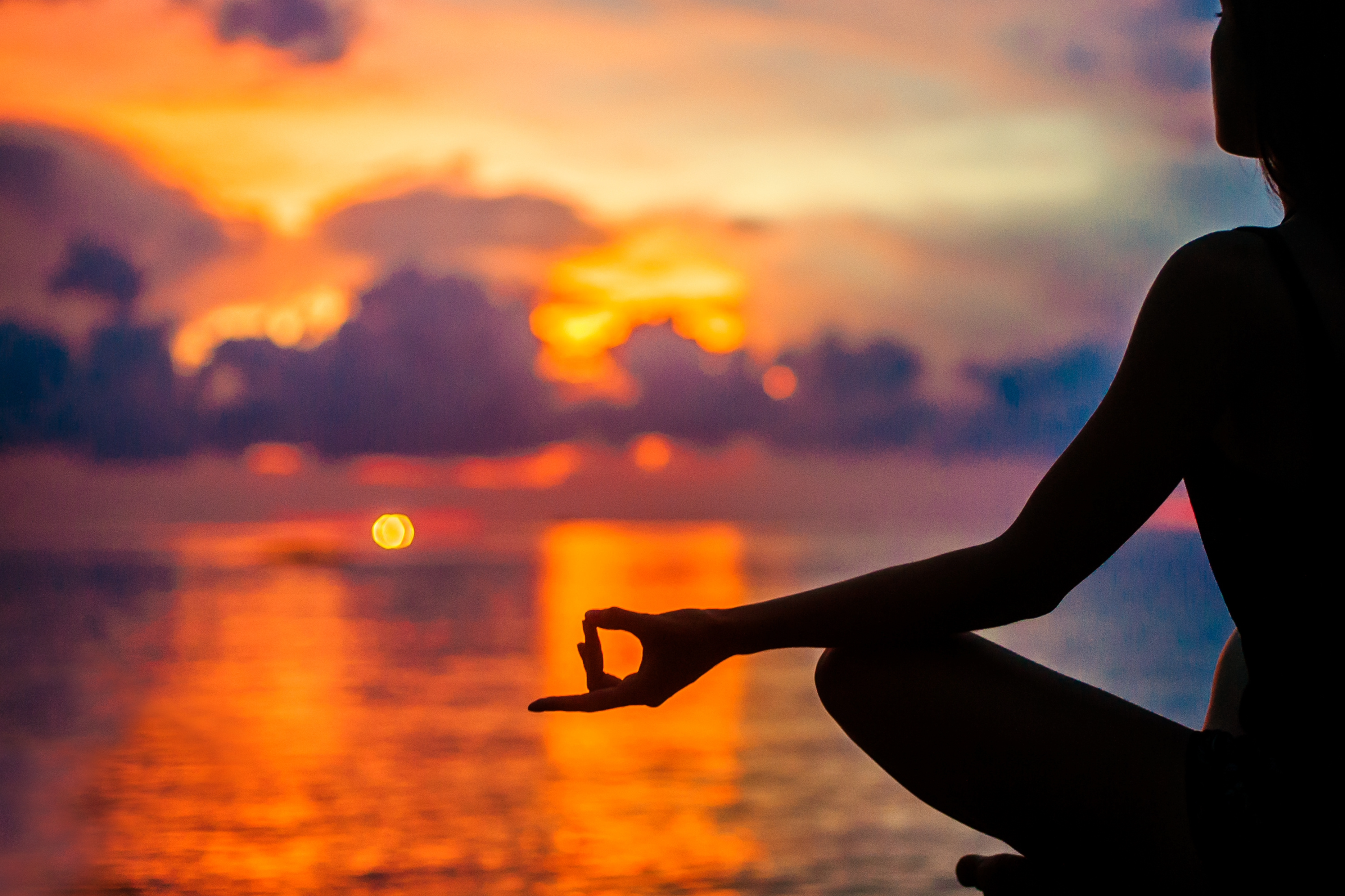 Silhouette of woman sitting in a peaceful yoga pose overlooking the ocean as the sun sets.